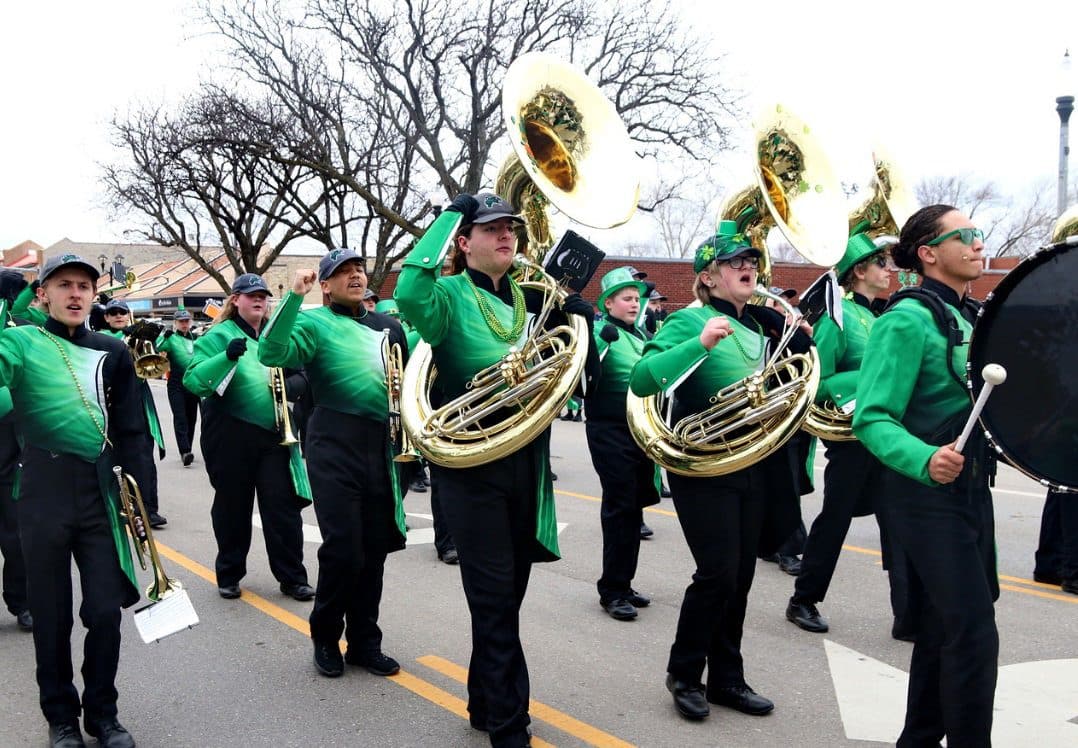 A marching band in green plays brass on the parade route