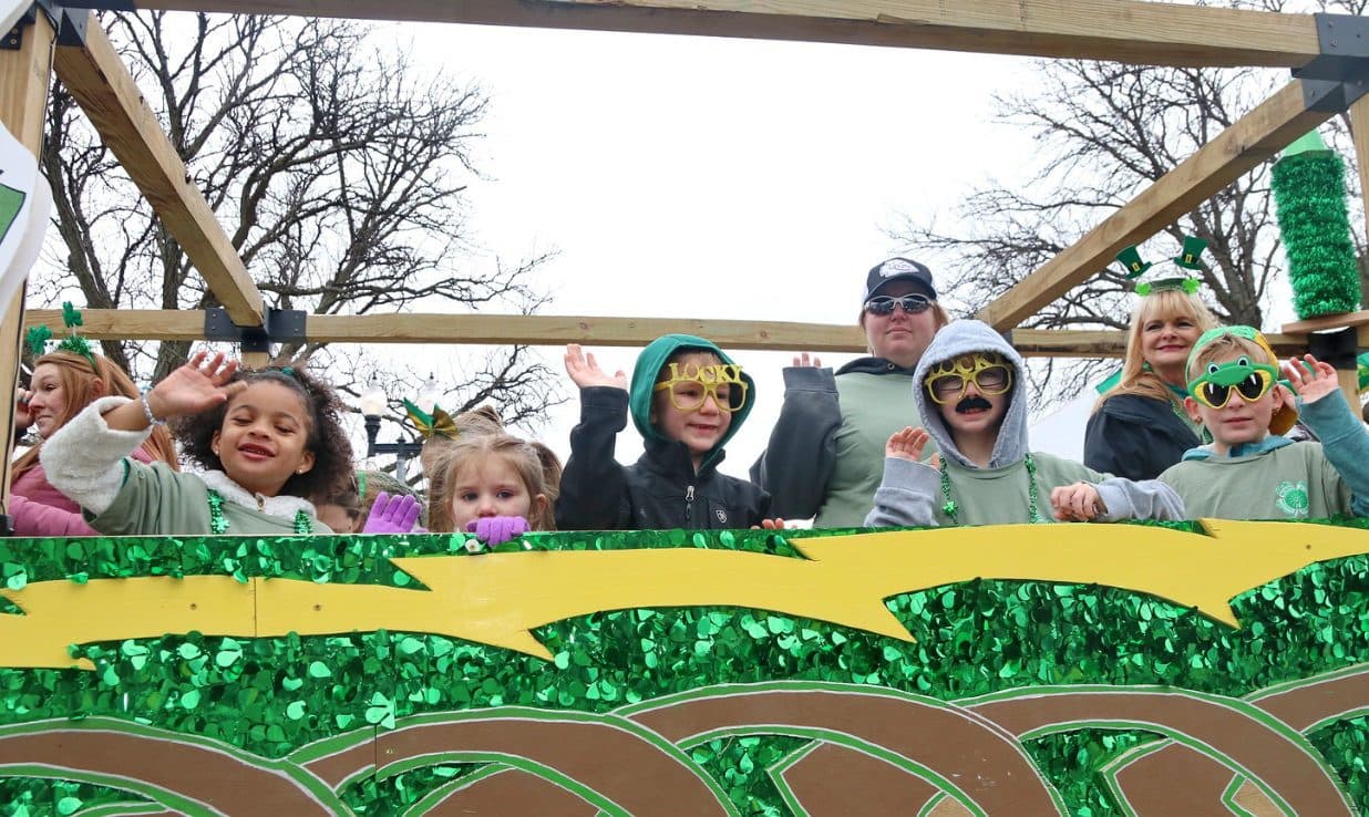 Kids waving from a green, glittering float on parade day