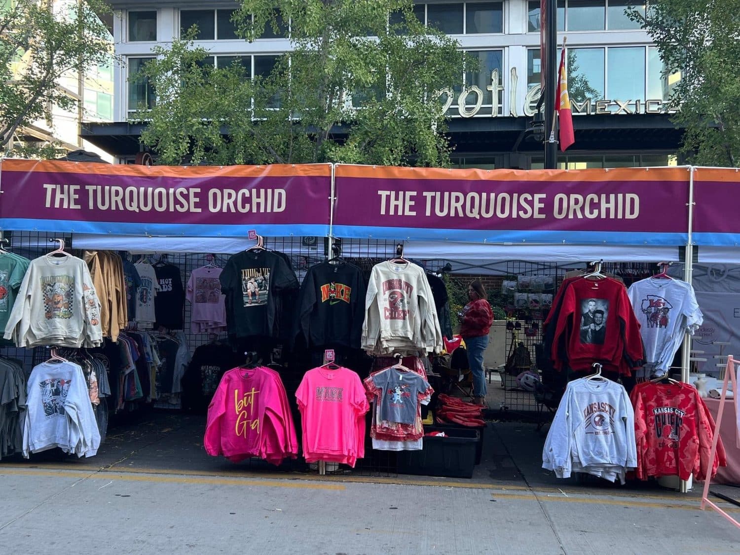 The Turquoise Orchid's vendor booth, racks of sweatshirts and T-shirts under a purple banner